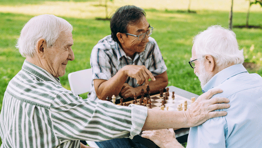Drei ältere Herren spielen im Park an einem Tisch Schach.
