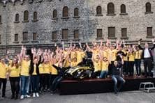 Eine Gruppe von rund 50 Studierenden in einheitlichen, gelben T_Shirts steht um einen schwarz-gelben Rennwagen und hebt die Hände jubelnd in die Höhe.