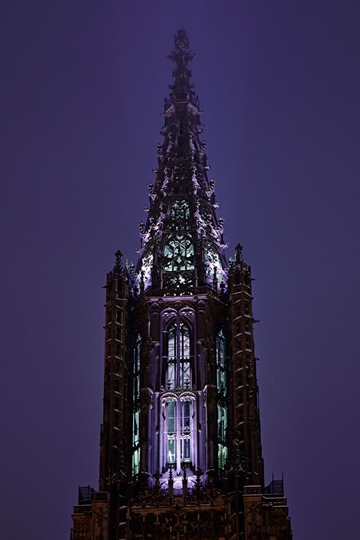 Im Turm des Münsters leuchtet Licht, das durch die offenen Fenster auch von draußen zu sehen ist.