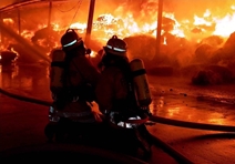 Angriffstrupp der Feuerwehr Ulm mit Schutzkleidung und Atemschutzgerät löscht mit einem C-Rohr aus 10 Meter Abstand eine im Vollbrand stehende Lagerhalle bei Nacht.
