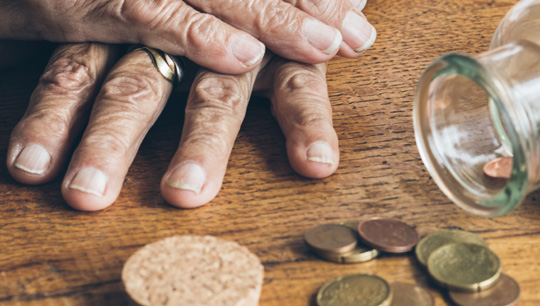Eine ältere Dame hat die Hände übereinandergelegt, vor ihr auf dem Tisch liegen ein paar Geldmünzen.
